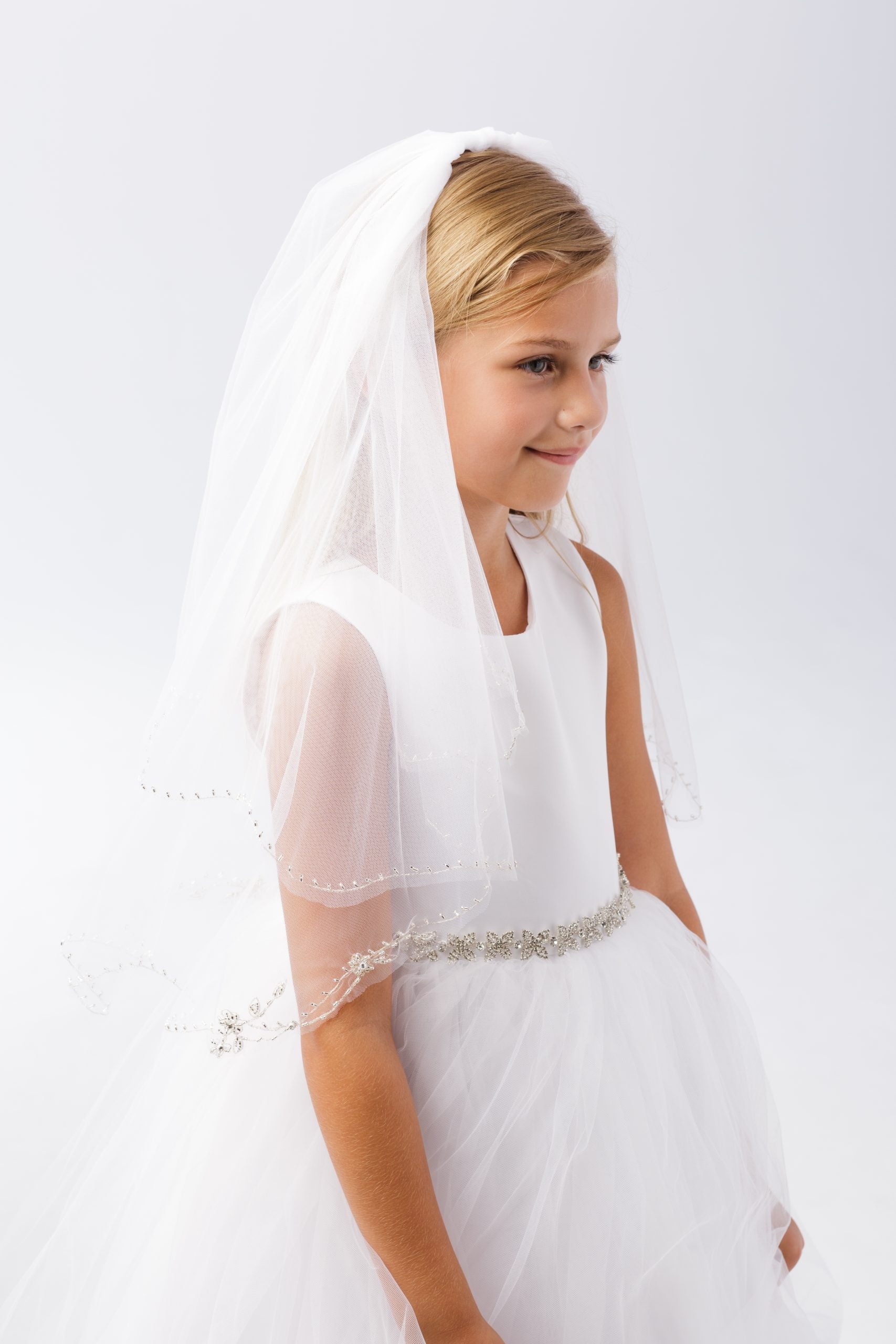698 Girl wearing a girls communion veil with beads, styled with a white dress for her special day.